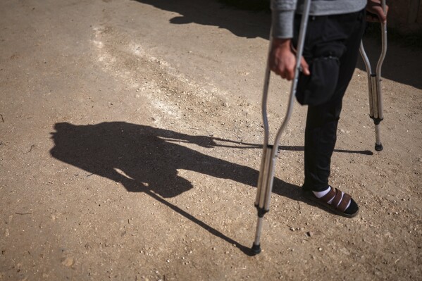 Suleiman Khalil, 21, who lost his leg in a landmine explosion while harvesting olives with his friends in a field, walks outside his home in the village of Qaminas, east of Idlib, Syria, Wednesday, April 9, 2025. (AP Photo/Ghaith Alsayed)