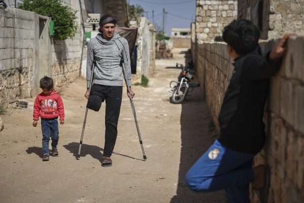 Suleiman Khalil, 21, who lost his leg in a landmine explosion while harvesting olives with his friends in a field, walks outside his home in the village of Qaminas, east of Idlib, Syria, Wednesday, April 9, 2025. (AP Photo/Ghaith Alsayed)