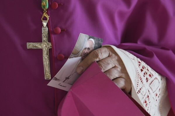 A prelate holds a picture of Pope Francis as he enters the atrium of St. Peter's Basilica at the Vatican, Wednesday, April 23, 2025, where the body of Pope Francis will lie in state for three days. (AP Photo/Andrew Medichini, Pool)