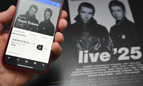 Smartphone with a booking site for Oasis tickets held in front of a promotional poster for the tour