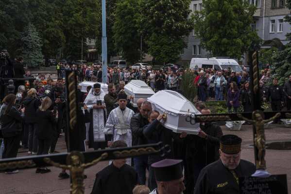 Funeral workers carry coffins during a funeral ceremony for Tamara Martyniuk, 8, Stanislav Martyniuk, 12, and Roman Martyniuk, 17, killed in a Russian strike on Sunday, in Korostyshiv, Zhytomyr region, Ukraine, Wednesday, May 28, 2025. (AP Photo/Evgeniy Maloletka)