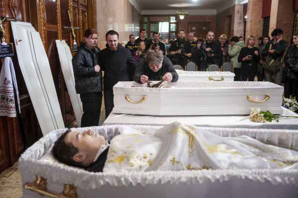 A father, center, mourns his children Tamara Martyniuk, 8, Stanislav Martyniuk, 12, and Roman Martyniuk, 17, killed in a Russian strike on Sunday, during farewell ceremony in Korostyshiv, Zhytomyr region, Ukraine, Wednesday, May 28, 2025. (AP Photo/Evgeniy Maloletka)