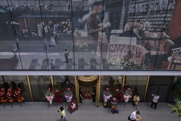 Workers wait for customer at a jewellry store as a projector screen promoting a newly opened outdoor Hutong style shopping mall, in Beijing, Monday, May 26, 2025. (AP Photo/Andy Wong)