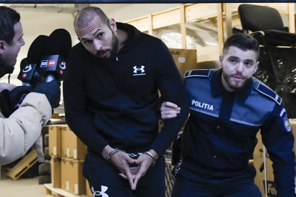 A police officer escorts Andrew Tate from the Directorate for Investigating Organized Crime and Terrorism (DIICOT) after prosecutors examined electronic equipment confiscated during the investigation in their case, in Bucharest, Romania, Jan. 25, 2023. (AP Photo/Alexandru Dobre, File)