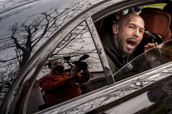 Andrew Tate speaks to media as he leaves in a vehicle after checking in at a police station as part of his judicial control, which requires him to appear before judicial authorities in Romania when summoned, in Voluntari, Romania, March 24, 2025. (AP Photo/Vadim Ghirda, File)