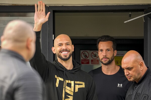 Andrew Tate waves next to his brother Tristan as they check in at a police station as part of their judicial control, which requires them to appear before judicial authorities in Romania when summoned, after returning from the United States, in Voluntari, Romania, March 24, 2025. (AP Photo/Vadim Ghirda)