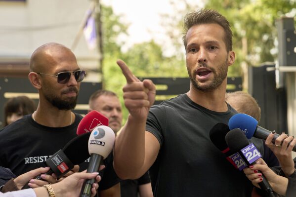 Andrew Tate, left, watches his brother Tristan speak, outside a police station in Voluntari, Romania, Wednesday, May 21, 2025. (AP Photo/Vadim Ghirda)