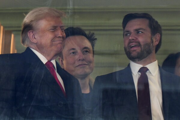 In this picture taken through a window, President-elect Donald Trump, from left, Trump's pick for the planned Department of Government Efficiency Elon Musk and Vice President-elect JD Vance attend the NCAA college football game between Army and Navy at Northwest Stadium in Landover, Md., Dec. 14, 2024. (AP Photo/Stephanie Scarbrough, File)